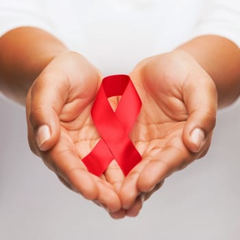 healthcare and medicine concept - female hands holding red AIDS awareness ribbon