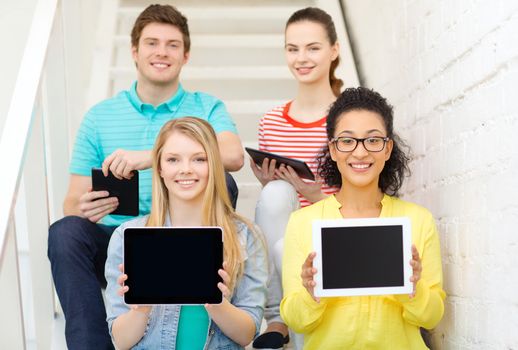 education and technology concept - smiling students showing tablet pc computer blank screen and sitting on staircase