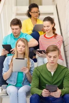 education and technology concept - busy students with tablet pc computer sitting on staircase