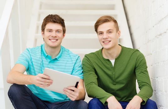 education and technology concept - smiling male students with tablet pc computer sitting on staircase