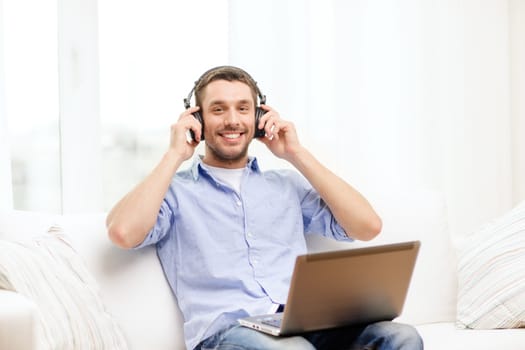 technology, home, music and lifestyle concept - smiling man with laptop and headphones at home