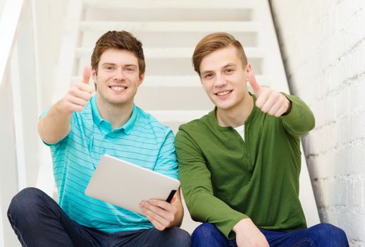 education and technology concept - smiling male students with tablet pc computer sitting on staircase