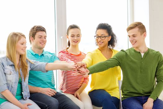 education and happiness concept - smiling students at school with hands on top of each