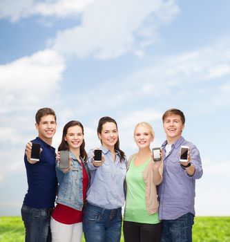 education and modern technology concept - smiling students showing blank smartphones screens