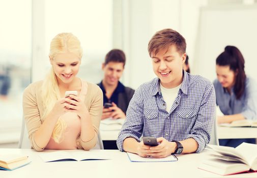 education and technology concept - group of students looking into smartphone at school