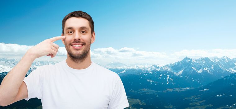 health and beauty concept - smiling young handsome man pointing to eyes