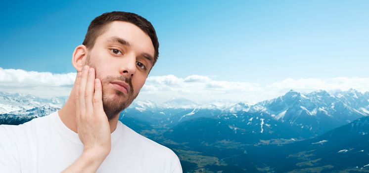 health and beauty concept - beautiful calm man touching his face