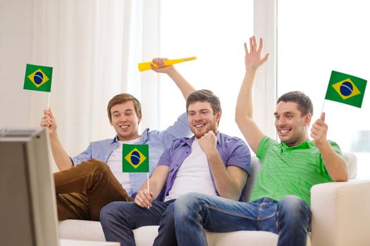 friendship, sports and entertainment concept - happy male friends with flags and vuvuzela supporting football team at home