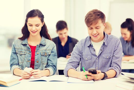 education and technology concept - group of students looking into smartphone at school