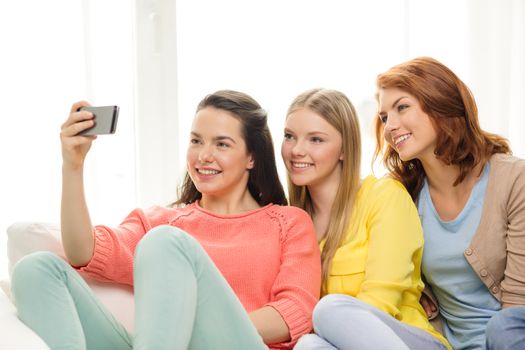 friendship, technology and internet concept - three smiling teenage girls taking picture with smartphone camera at home