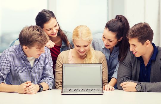 education, technology, advertisement and internet concept - group of smiling students looking at blank black laptop screen