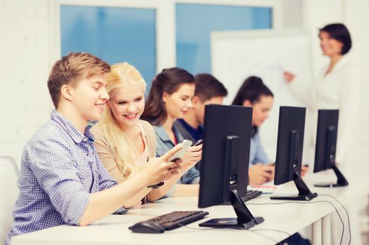 education, technology and internet concept - students with computer monitor and smartphones