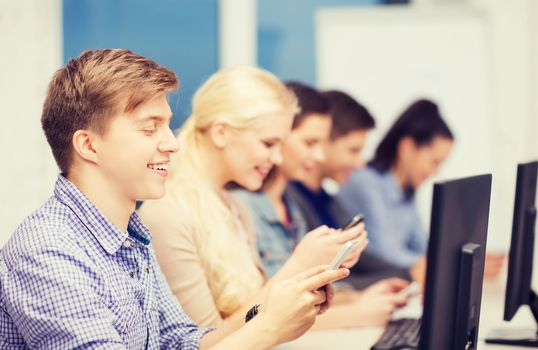 education, technology and internet concept - students with computer monitor and smartphones