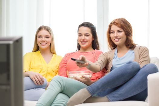 home, technology and friendship concept - three smiling teenage girl watching tv at home and eating popcorn