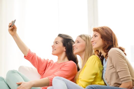 friendship, technology and internet concept - three smiling teenage girls taking picture with smartphone camera at home