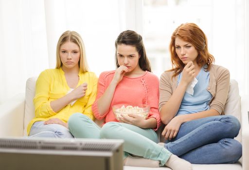 home, technology and friendship concept - three sad teenage girl watching tv at home and eating popcorn