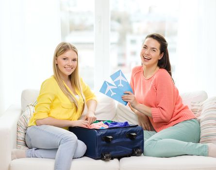 travel, vacation and friendship concept - two smiling teenage girls with plane tickets and packed suitcase