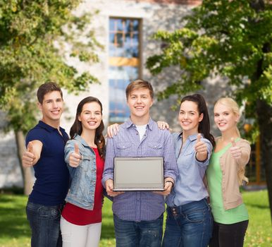 education, advertisement and new technology concept - smiling students with laptop computer blank screen showing thumbs up