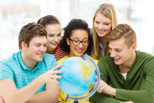 education, travel and geography concept - five smiling student looking at earth globe at school