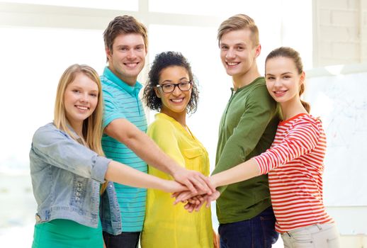 education and friendship concept - five smiling students with hands on top of each other