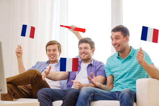 friendship, sports and entertainment concept - happy male friends with flags and vuvuzela supporting football team at home