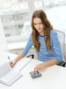 education and home concept - concentrated student girl with notebook, calculator and book