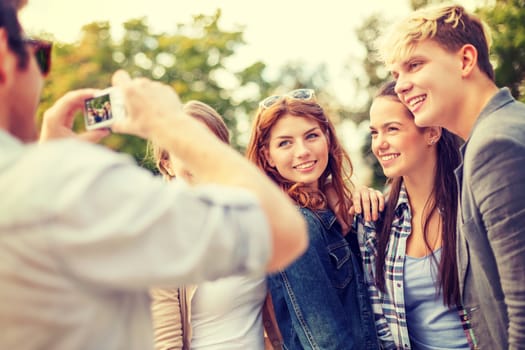 summer holidays, electronics and teenage concept - group of smiling teenagers taking photo with digital camera outside