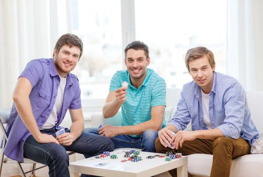leisure, games and lifestyle concept - happy three male friends playing poker at home
