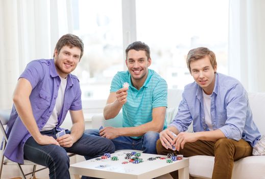 leisure, games and lifestyle concept - happy three male friends playing poker at home