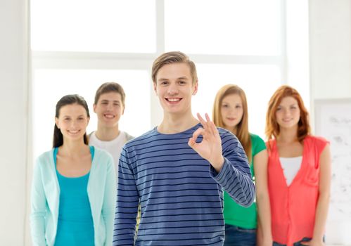 education, gesture and school concept - group of smiling students with teenage boy in front showing ok sign