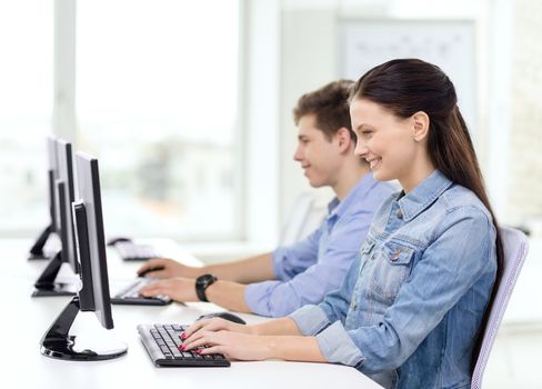 education, technology and school concept - two smiling students in computer class