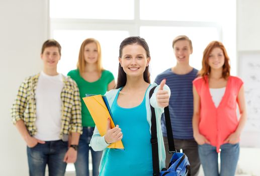 education and school concept - group of smiling students with teenage girl in front with bag and folders showing thumbs up