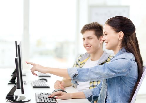 education, technology and school concept - two smiling students in computer class, girl pointing finger at screen