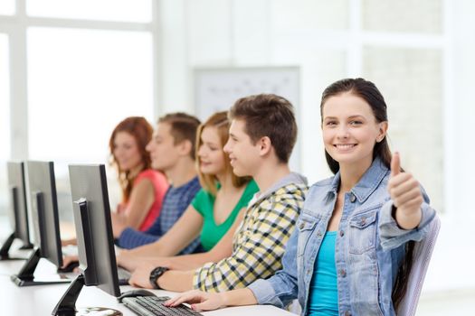 education, technology and school concept - smiling female student with classmates in computer class at school showing thumbs up