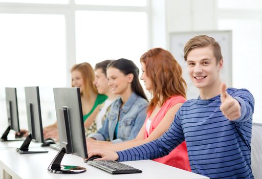 education, technology and school concept - smiling male student with classmates in computer class at school showing thumbs up