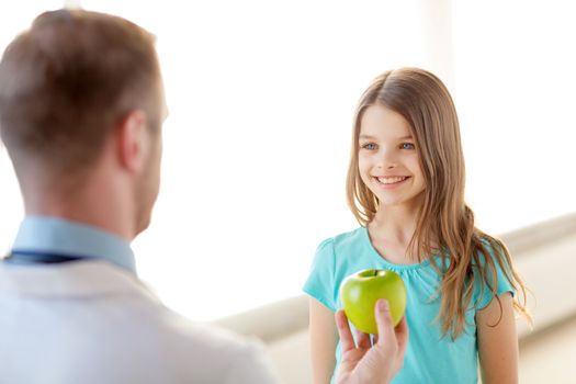 healthcare, child and medicine concept - male doctor giving an apple to smiling little girl