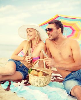 summer, holidays, vacation and happy people concept - smiling couple having picnic on the beach under colorful umbrella