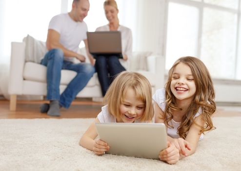 family, children, technology and home concept - smiling sister with tablet pc computer and parents on the back with laptop