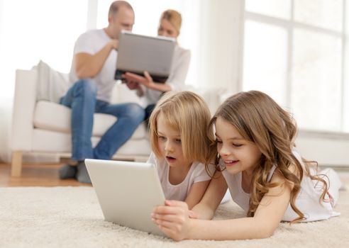 family, children, technology and home concept - smiling sister with tablet pc computer and parents on the back with laptop