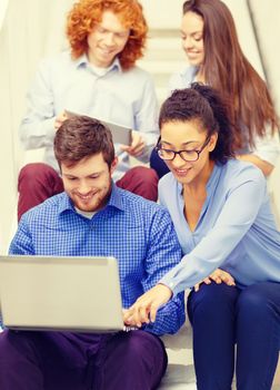 business, technology and startup concept - smiling creative team with laptop and tablet pc computer sitting on staircase