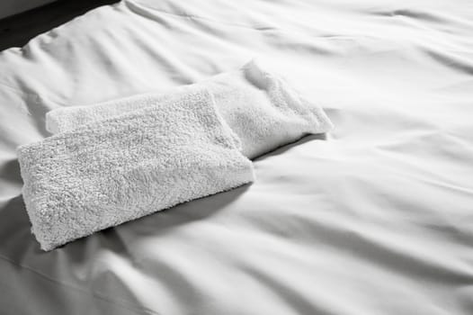 White hotel towels on white bed. Black and white picture.