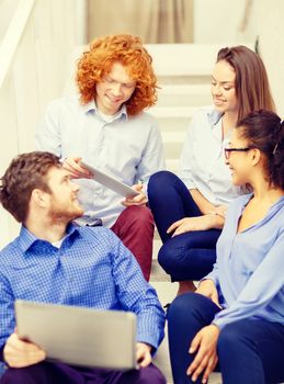 business, technology and startup concept - smiling creative team with laptop and tablet pc computer sitting on staircase