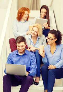 business, technology and startup concept - smiling creative team with laptop and tablet pc computer sitting on staircase