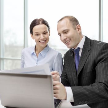 business, technology and office concept - businessman and businesswoman with laptop computer and papers having discussion in office