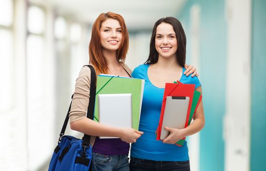 education, technology and people concept - two smiling students with bag, folders and tablet pc standing