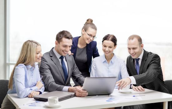 business, technology and office concept - smiling business team with laptop computers, documents and coffee having discussion in office