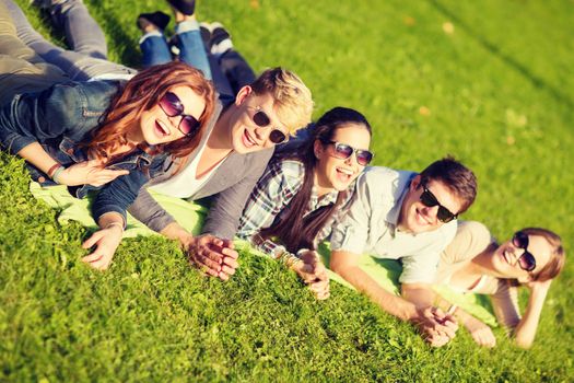 summer holidays, education and teenage lifestyle concept - group of students or teenagers lying on grass in park