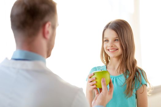 healthcare, child and medicine concept - male doctor giving an apple to smiling little girl