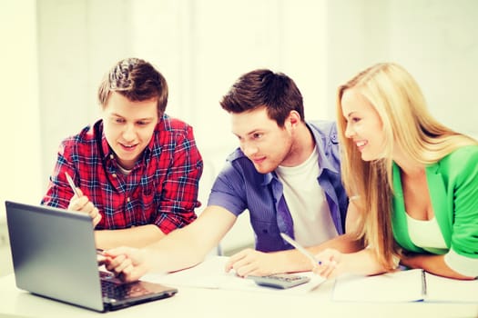 education concept - smiling students looking at laptop at school