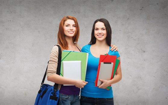 education, technology and people concept - two smiling students with bag, folders and tablet pc standing